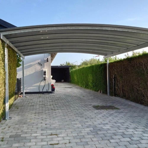Lang dobbelt carport med buet tag og oplader langs indkørsel
