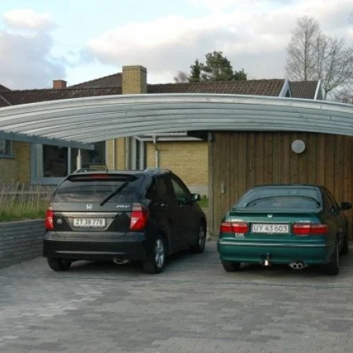 Dobbelt carport med plads til to biler foran gult murstenshus