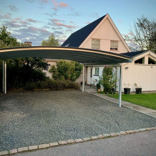 Dobbelt carport med buet tag ved villa og grusindkørsel i Dragør