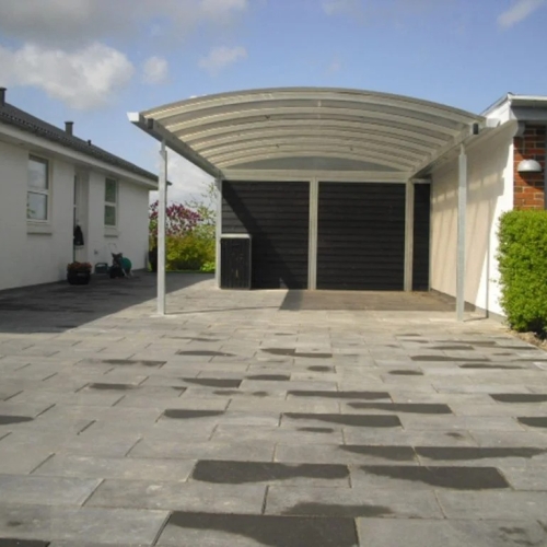 Moderne carport med skur og buet tag ved flisebelagt gårdsplads i Aalborg