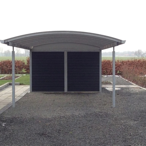 Carport med skur i mørkt træ og buet tag på grusbelagt indkørsel i Aarhus