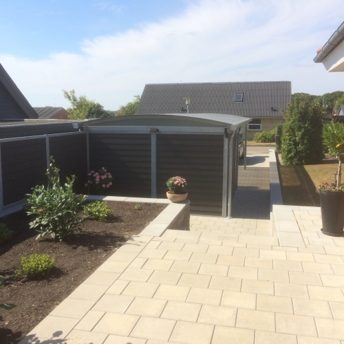Carport med skur og buet tag integreret i velanlagt have i Frederikshavn.