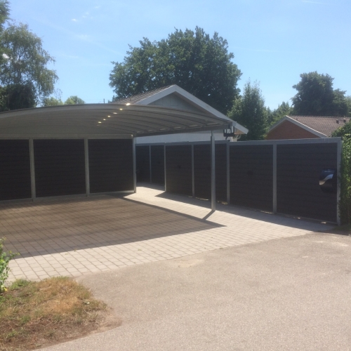 Stor carport med skur og integreret hegn i mørke træelementer i Solrød Strand