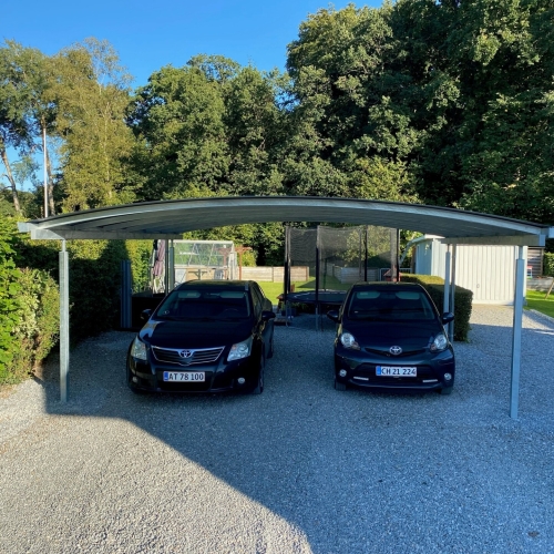 Dobbelt carport i stål med buet tag og grusbelagt indkørsel