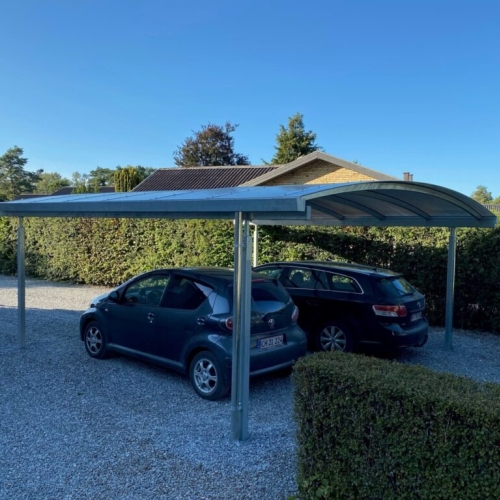 Fritstående dobbelt carport med buet tag og parkeringsplads til to biler