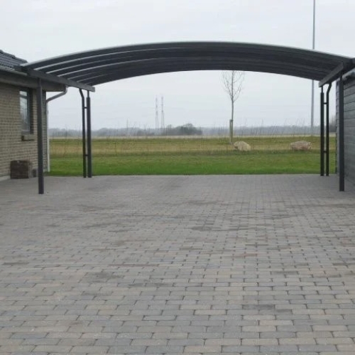 Sort dobbelt carport med buet tag på flisebelagt indkørsel