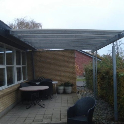 Smal terrasseoverdækning langs husfacade med siddepladser