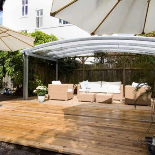 Buet terrasseoverdækning over stor træterrasse med lounge