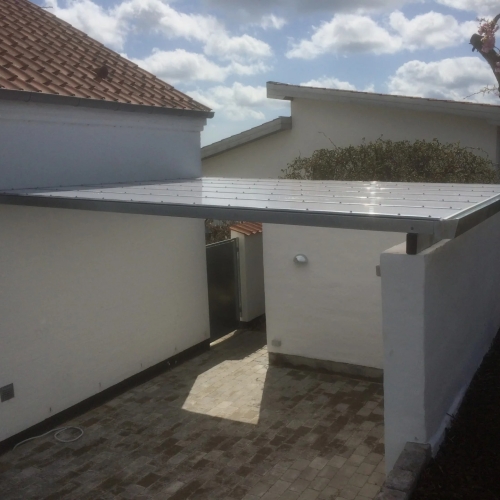 Moderne terrasseoverdækning og carport mellem bygninger med flisebelægning